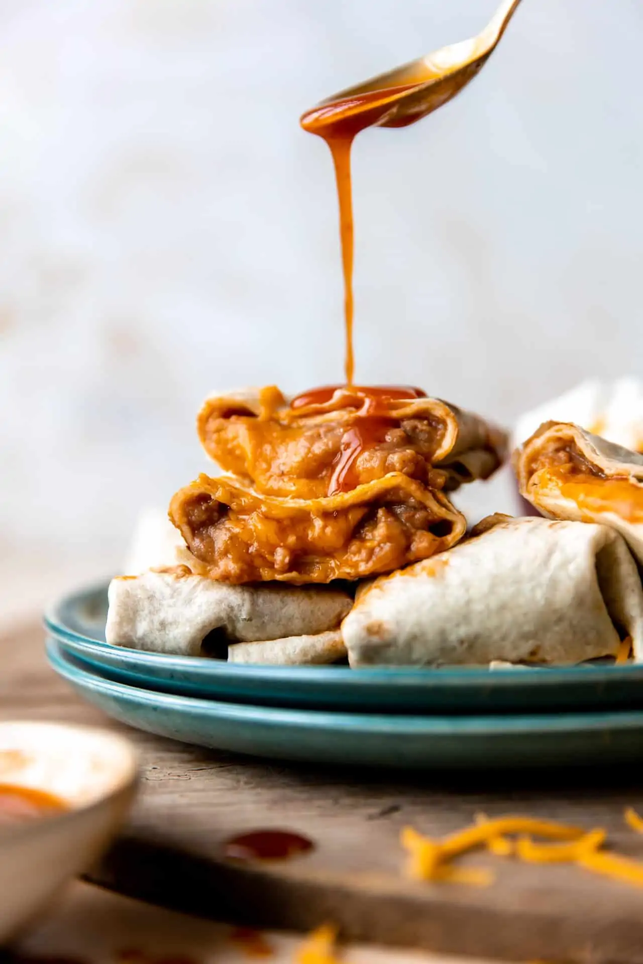 Sauce being poured over the top of a stack of bean and cheese burritos.