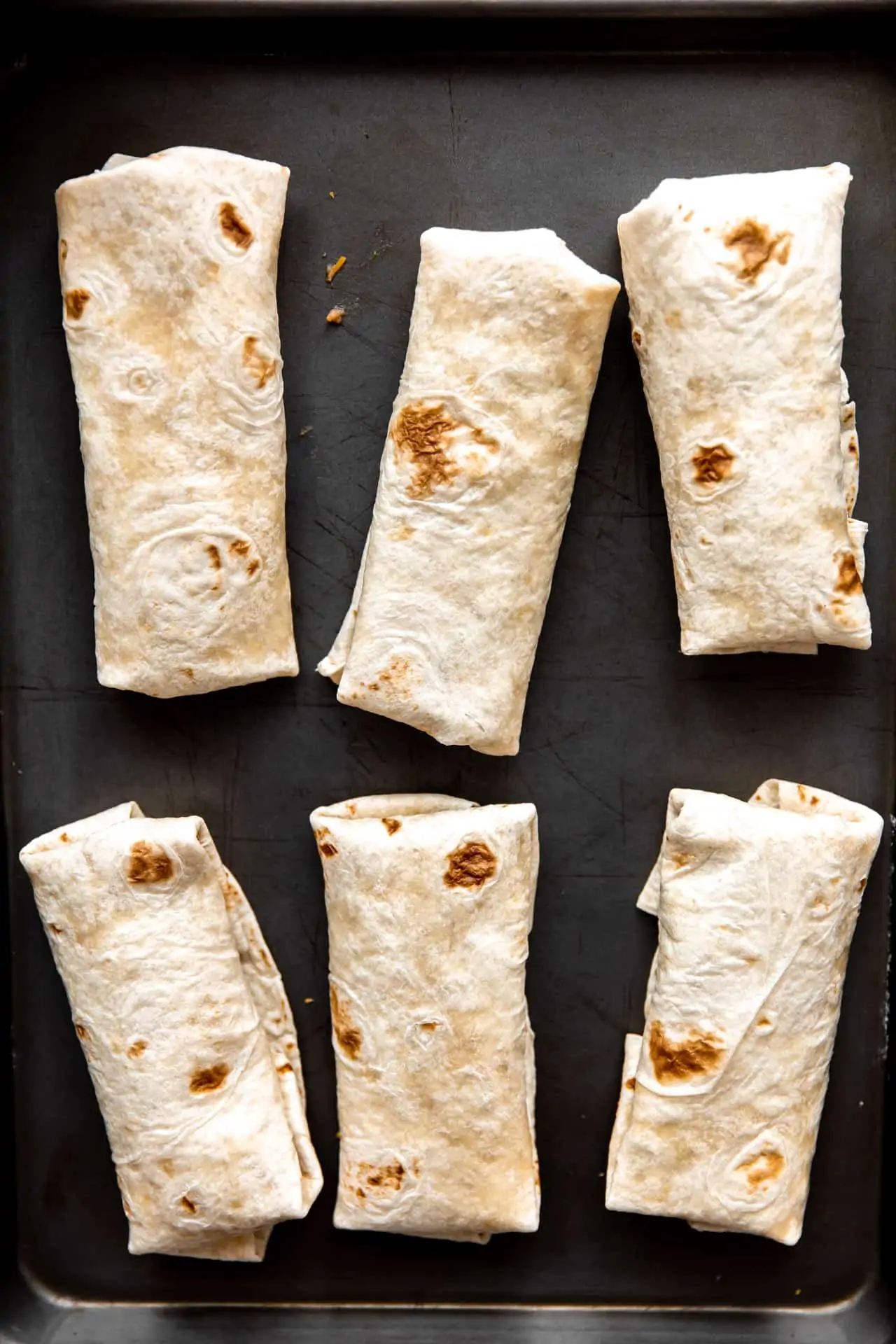 burritos laid out on a baking sheet to bake. 
