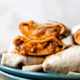 Bean and cheese burritos stacked on a plate showing melty cheese and creamy beans with red sauce inside.