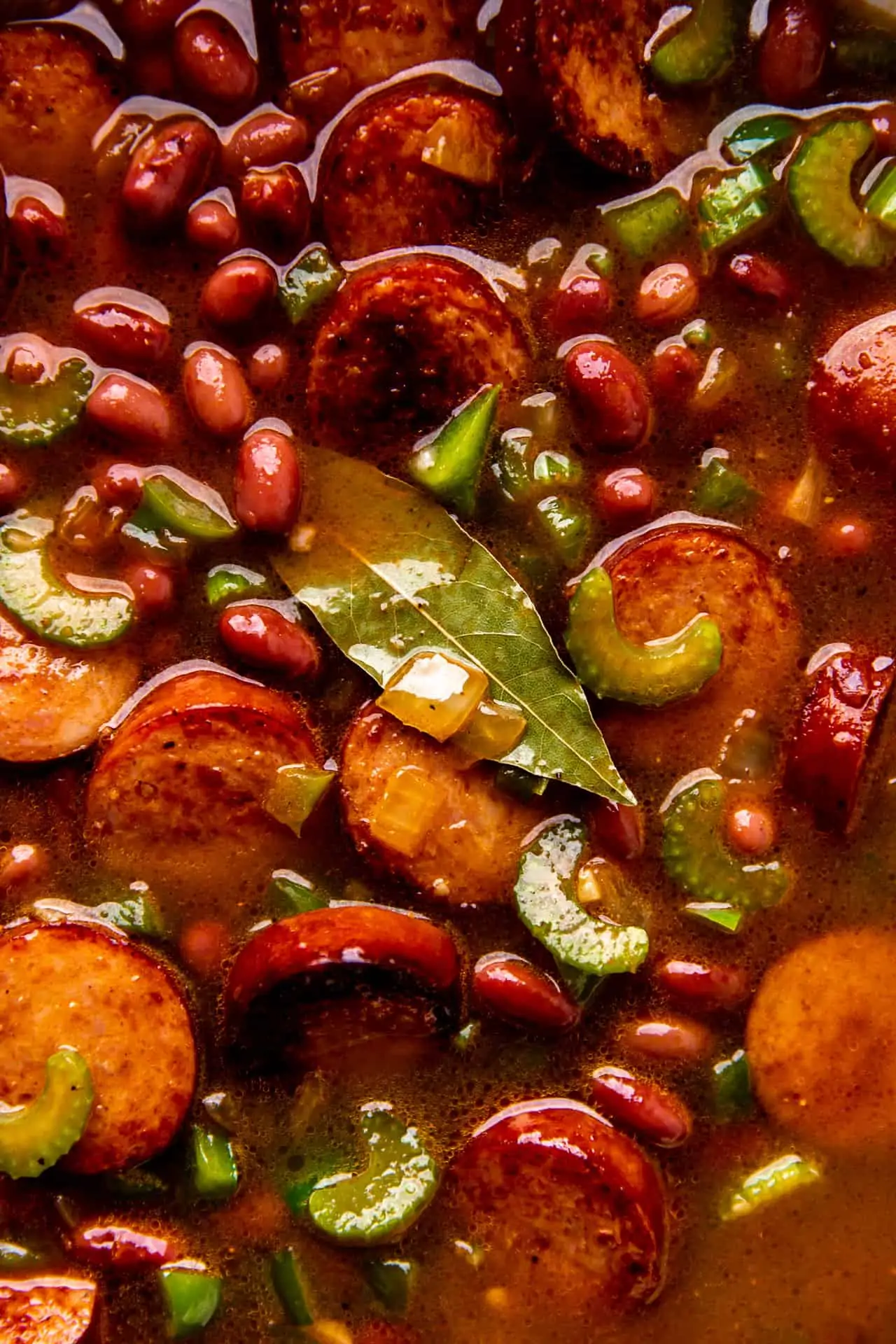 Cooked red beans and rice close up shot showing a thick spicy broth with seared sausage and veggies.