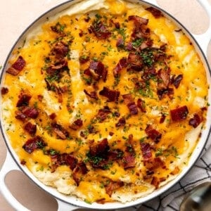Round baking dish with baked mashed potato casserole, topped with melty cheese, crisp bacon and green chives.