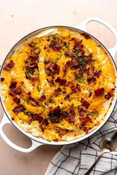 Round baking dish with baked mashed potato casserole, topped with melty cheese, crisp bacon and green chives.