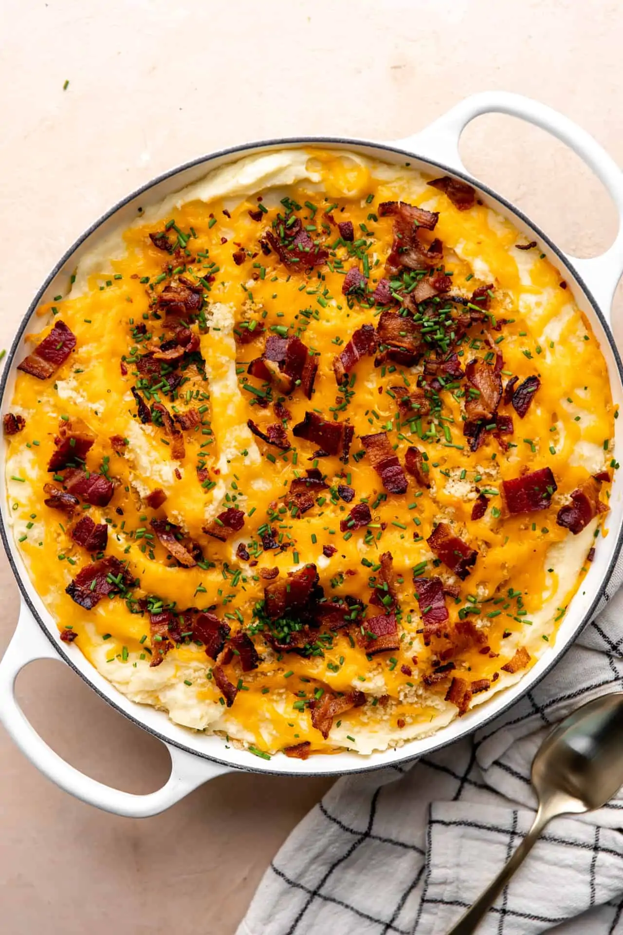 Round baking dish with baked mashed potato casserole, topped with melty cheese, crisp bacon and green chives.