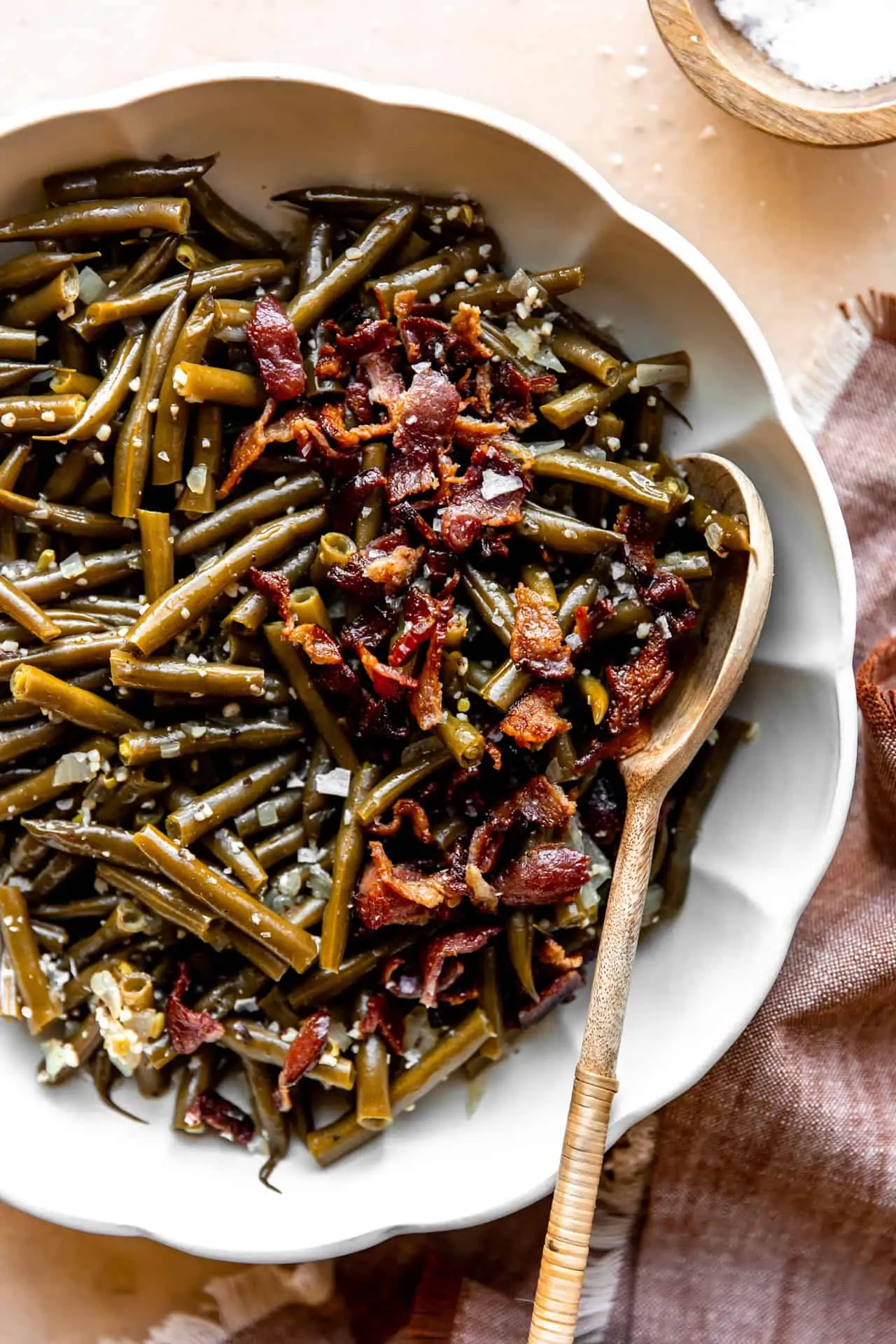 Bowl served with southern green beans topped with crispy bacon and a wooden spoon for serving.