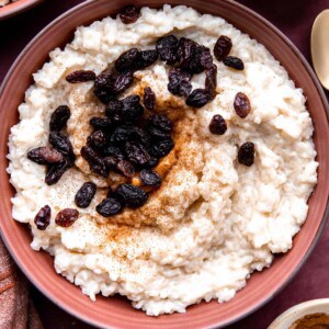 Bowl of creamy rice pudding topped with raisins and a sprinkle of cinnamon.