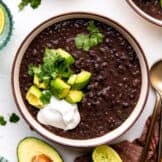 Bowl of black bean soup topped with diced avocado, sour cream and fresh cilantro.