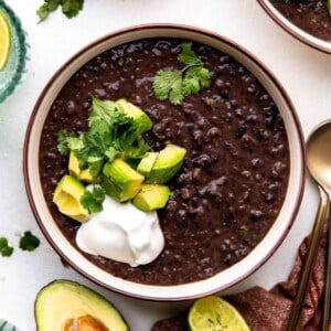 Bowl of black bean soup topped with diced avocado, sour cream and fresh cilantro.