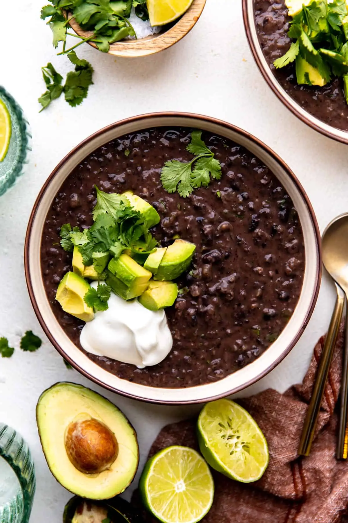 Bowl of black bean soup topped with diced avocado, sour cream and fresh cilantro.