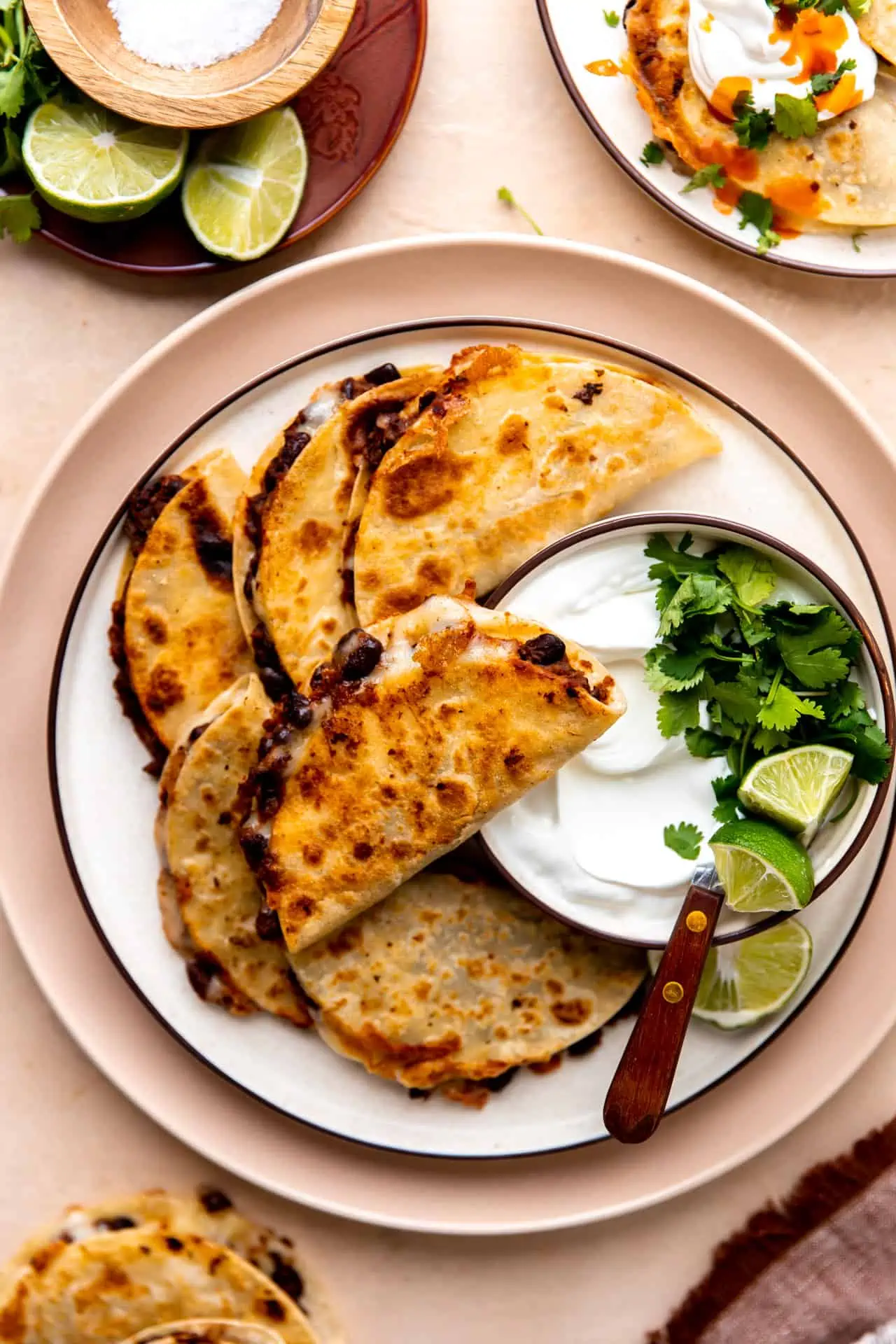 Plate filled with crispy black bean tacos served with a bowl of sour cream, cilantro and lime. 