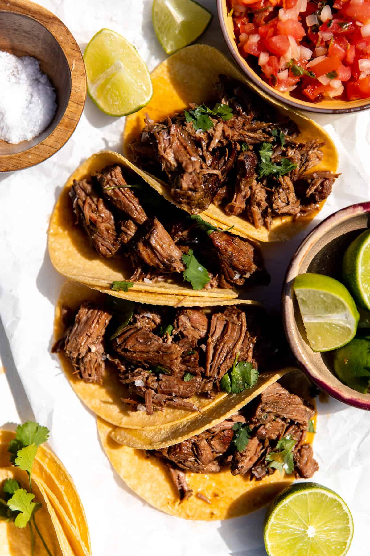 Shredded beef tacos laid out in the sun with pico, limes and cilantro. 
