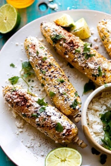 Plate of elotes served with extra crumbled cotija, lime wedges and fresh cilantro.