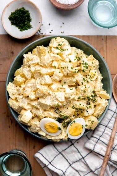 Bowl of creamy potato salad made with egg and dill pickle. Topped with sliced apart hard boiled egg.