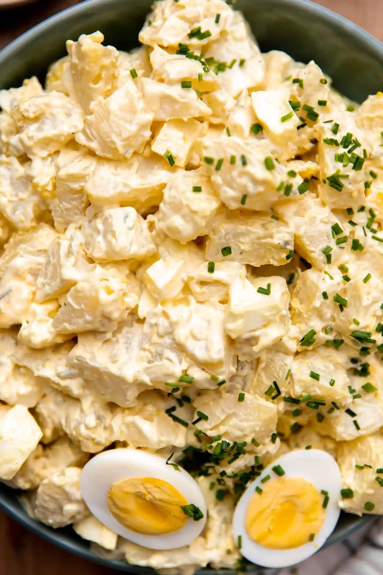 Close up view of creamy southern potato salad topped with diced chives and hard boiled egg. 