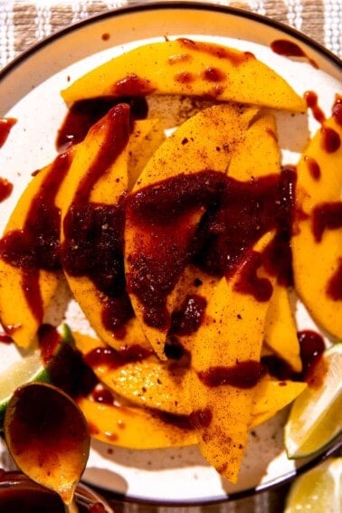 Plate with sliced mango, drizzled in chamoy and sprinkled with tajin.