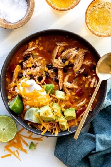Bowl of chicken enchilada soup topped with cheese, sour cream and avocado.