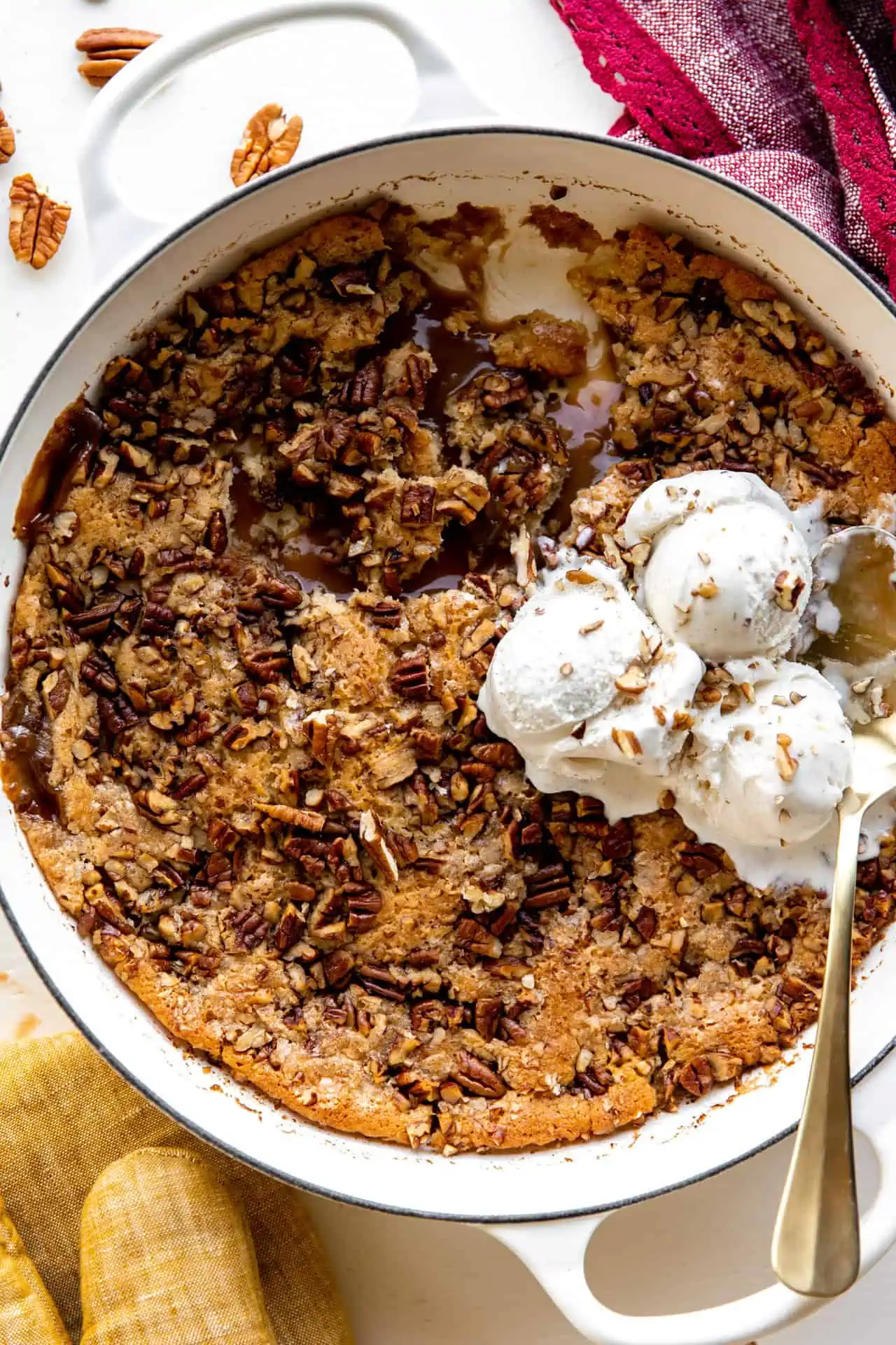 baking dish with pecan cobbler showing caramel sauce and topped with ice cream.