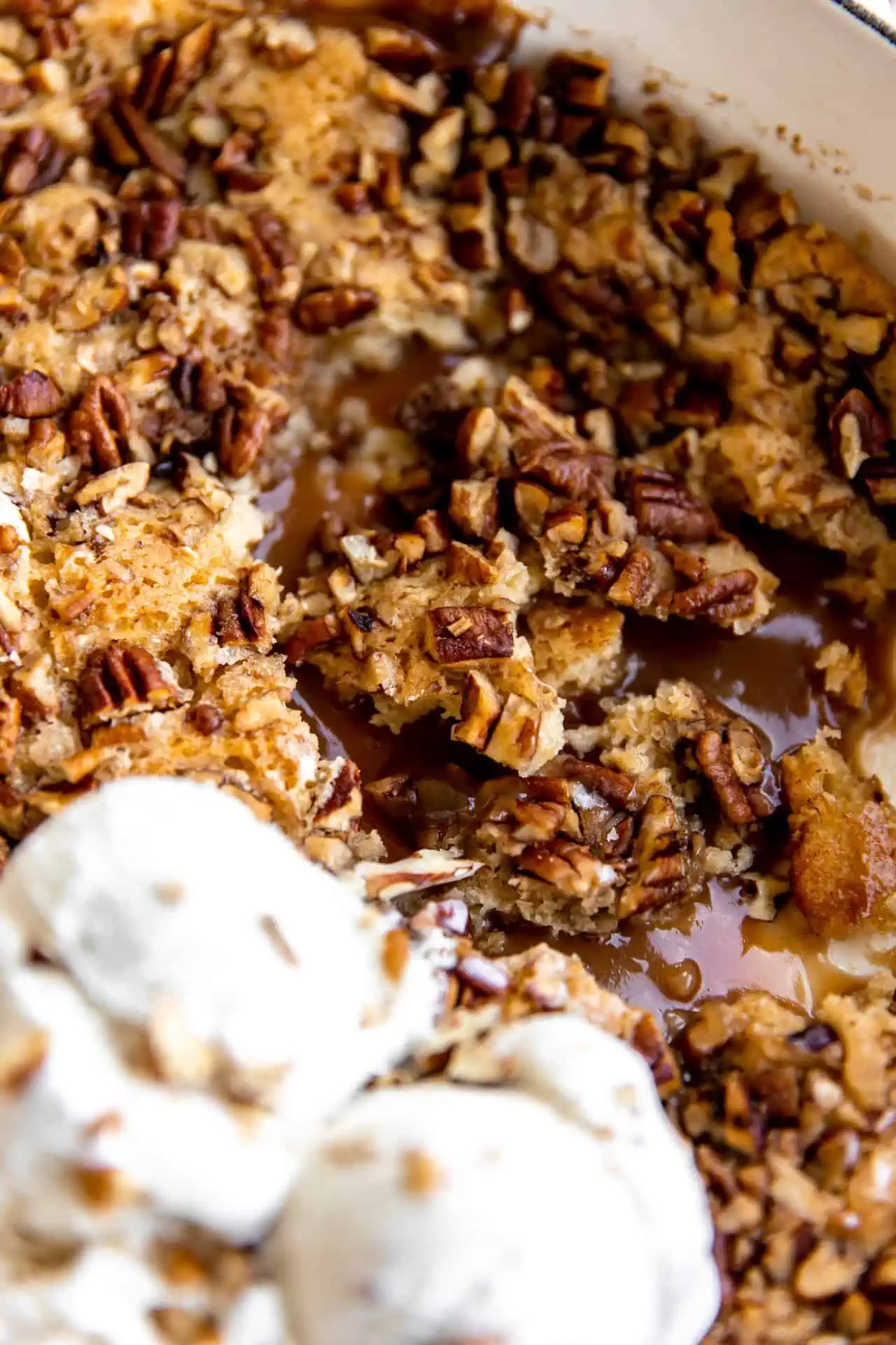 Up close view of gooey caramel pecan filling topped with crunchy cobbler topping and served with ice cream. 