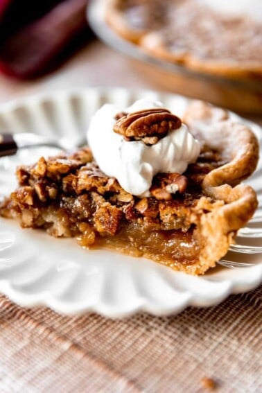 Slice of pecan pie topped with a swirl of whipped cream and a halved pecan on top.