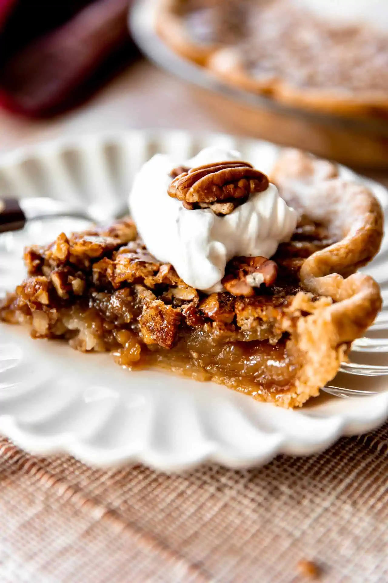 Slice of pecan pie topped with a swirl of whipped cream and a halved pecan on top.