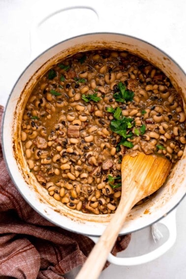 Pot filled with cooked black eyed peas with chunks of ham and bacon, topped with cilantro.