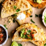 Overhead of several crispy fried potato tacos topped with sour cream, guacamole and salsa.