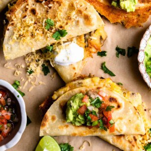 Overhead of several crispy fried potato tacos topped with sour cream, guacamole and salsa.