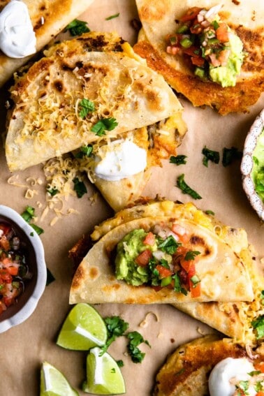 Overhead of several crispy fried potato tacos topped with sour cream, guacamole and salsa.
