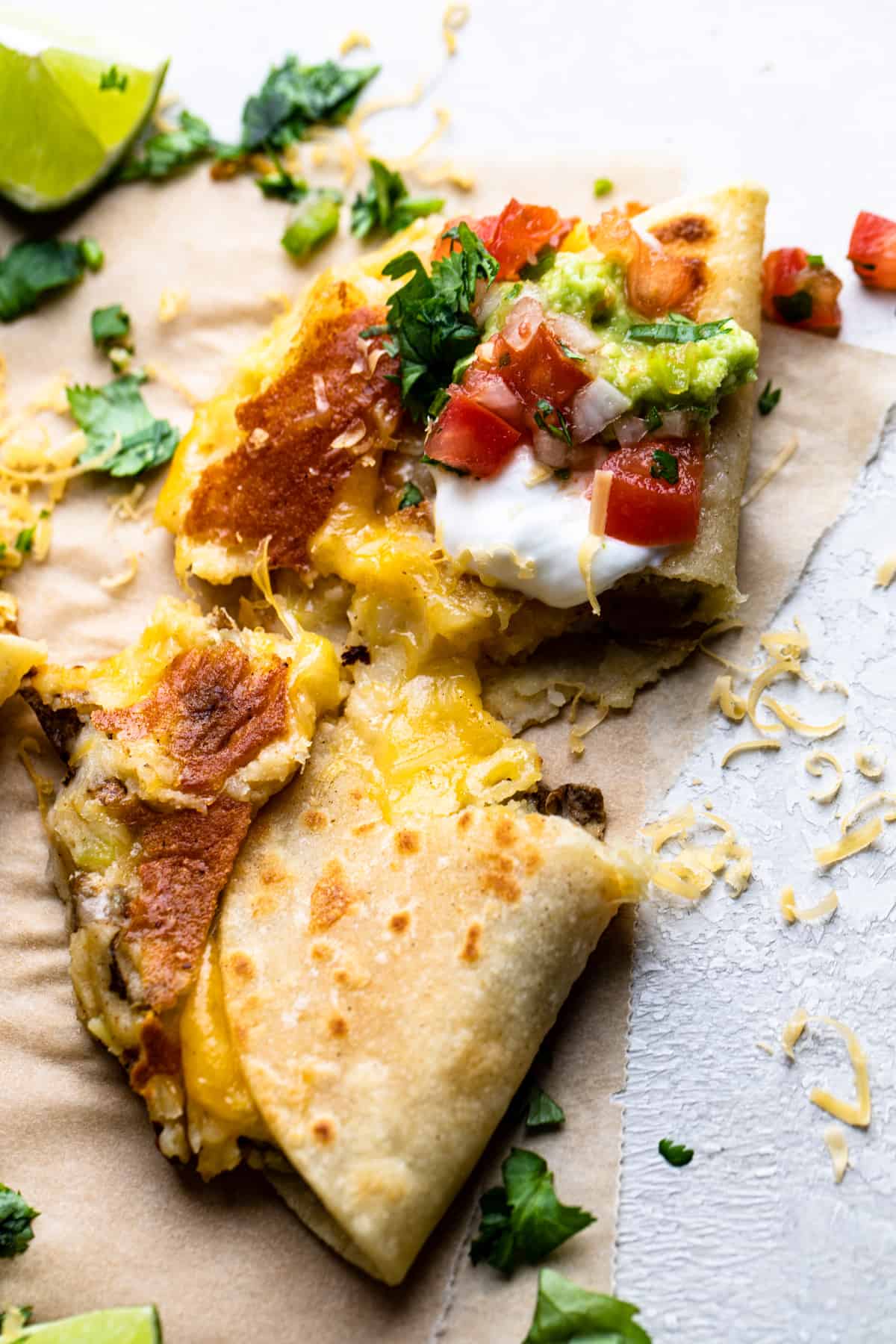 Crispy Mexican Potato Taco split in half showing melty cheese and topped with sour cream, guacamole and salsa.