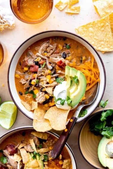 Bowl of chicken taco soup topped with tortilla chips, sour cream and sliced avocado.