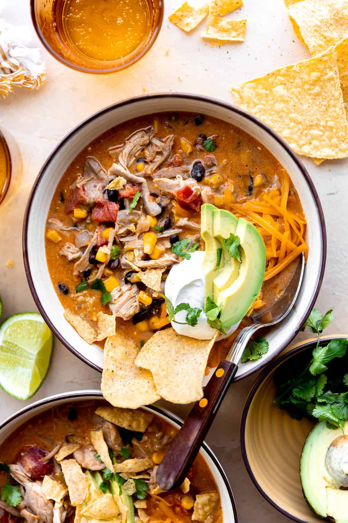 Bowl of chicken taco soup topped with tortilla chips, sour cream and sliced avocado.