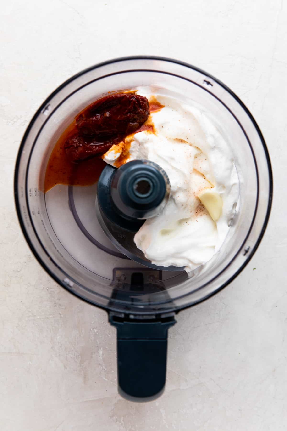 Food processor with ingredients needed to make chipotle crema before blending. 