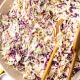 Bowl filled with a creamy southern coleslaw served with wooden spoons.