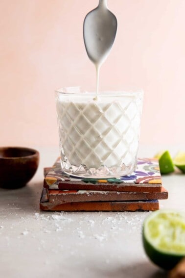 Cup filled with homemade mexican crema with a spoon above drizzling crema.