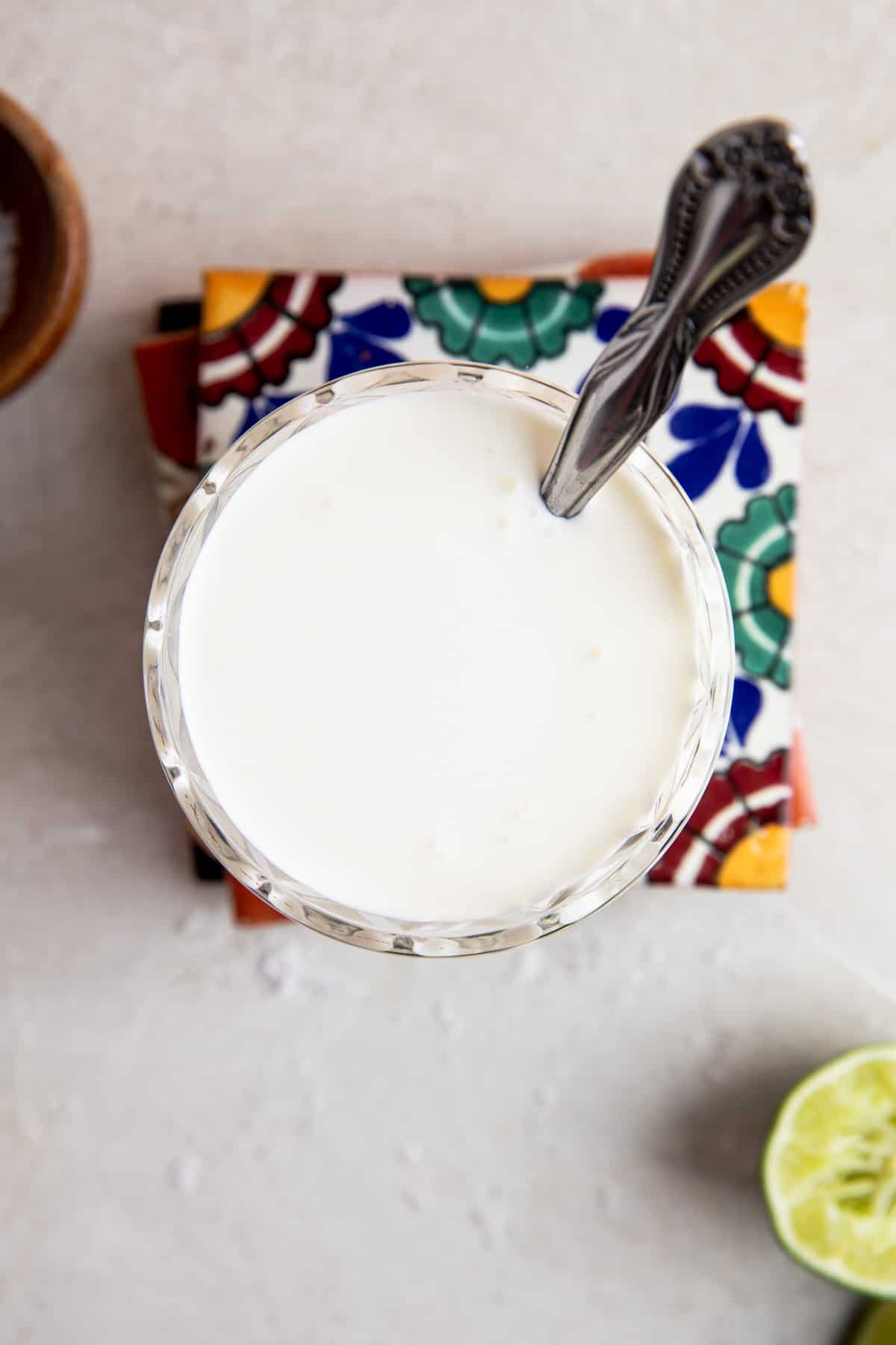 Overhead of a glass filled with mexican cream sauce with a spoon dipping in. 