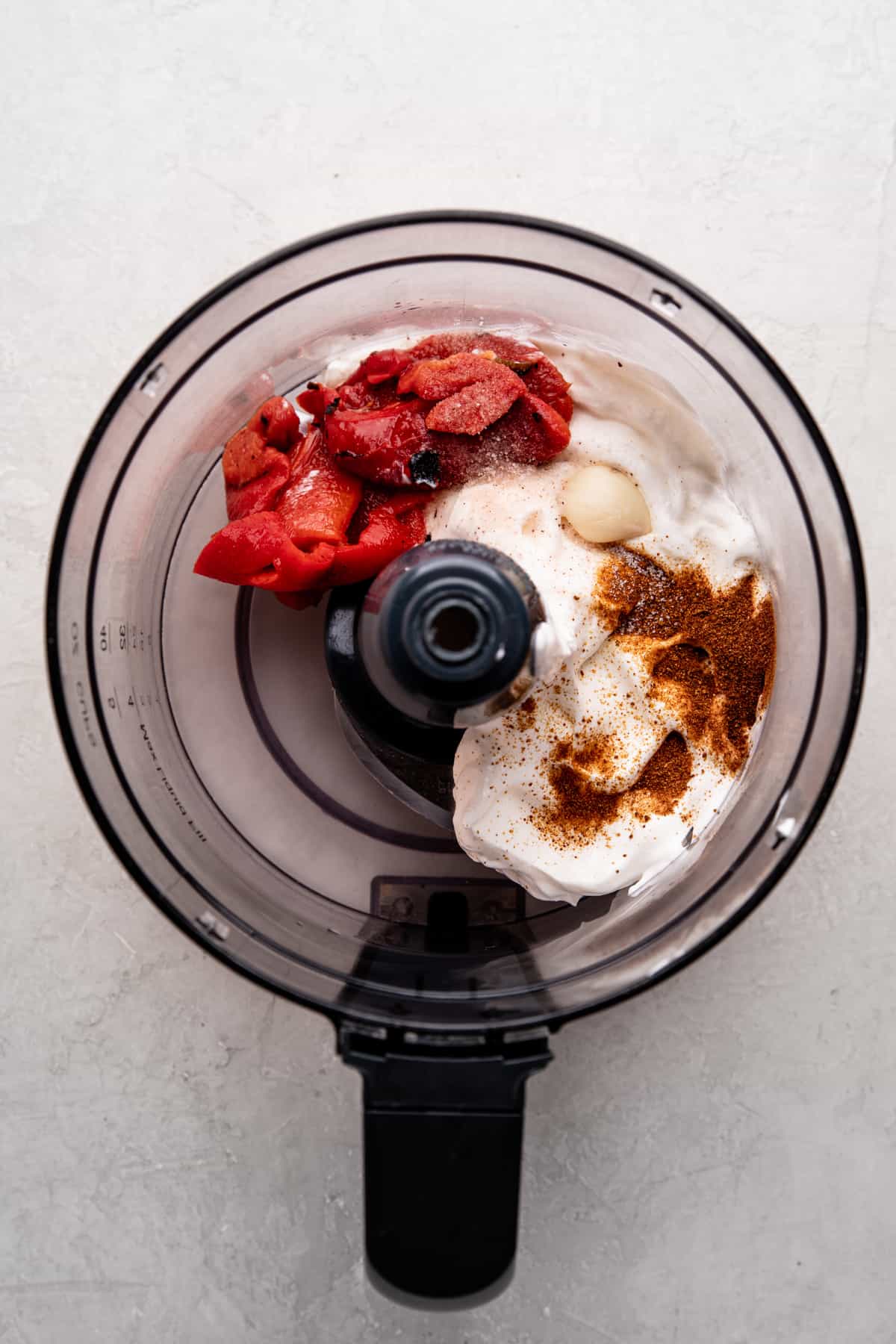 Food processor filled with ingredients for smoky red pepper crema before being blended.