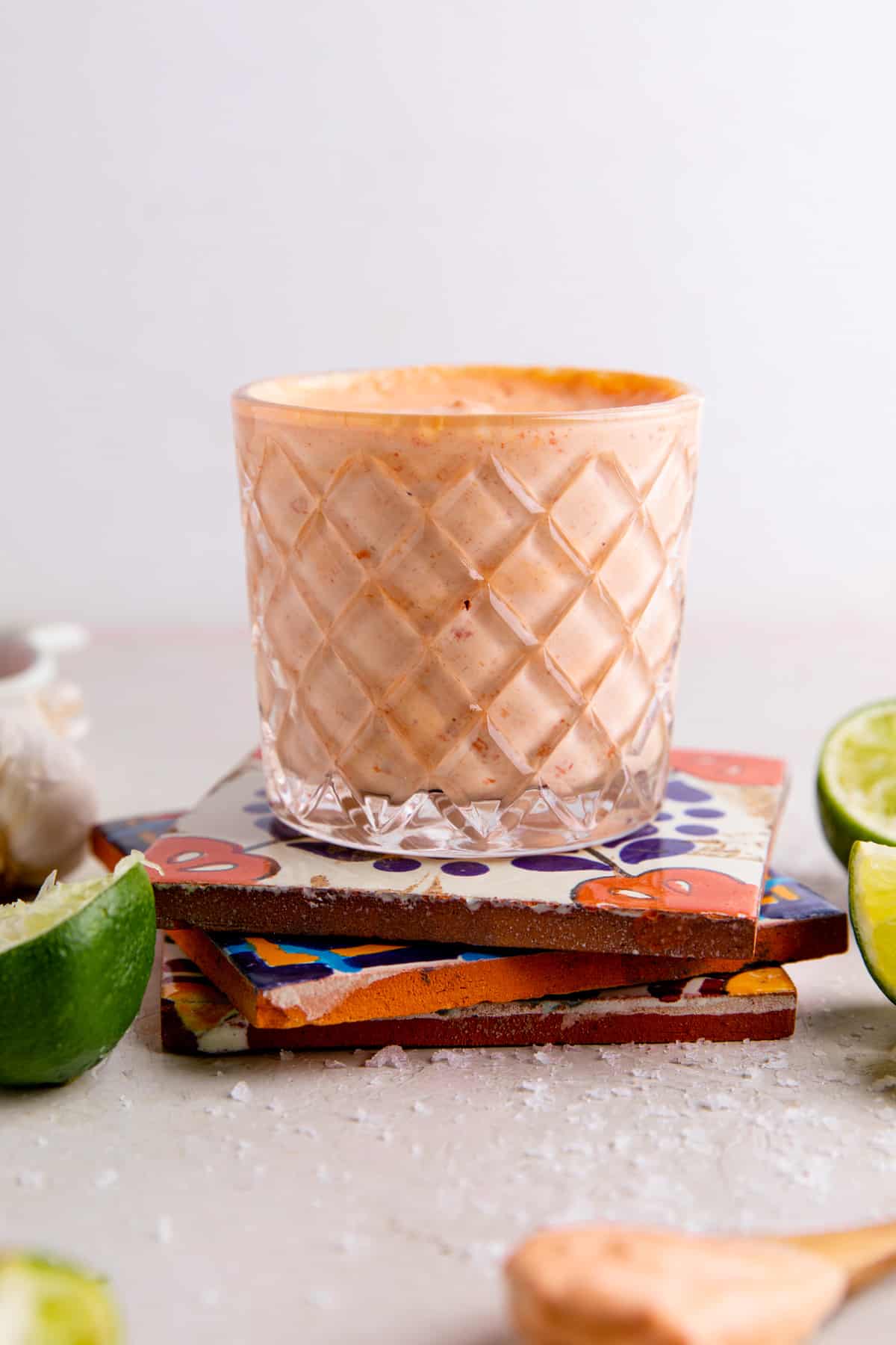 Glass of red pepper crema on top of mexican tiles, lime wedges on the side. 