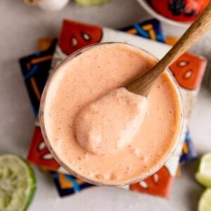 Glass filled with red pepper crema with a wooden spoon scooping it up.