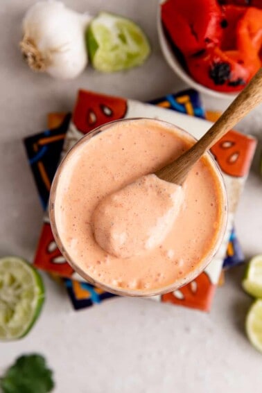 Glass filled with red pepper crema with a wooden spoon scooping it up.