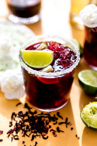 Hibiscus margarita in a glass rimmed with sugar and garnished with a lime wedge.