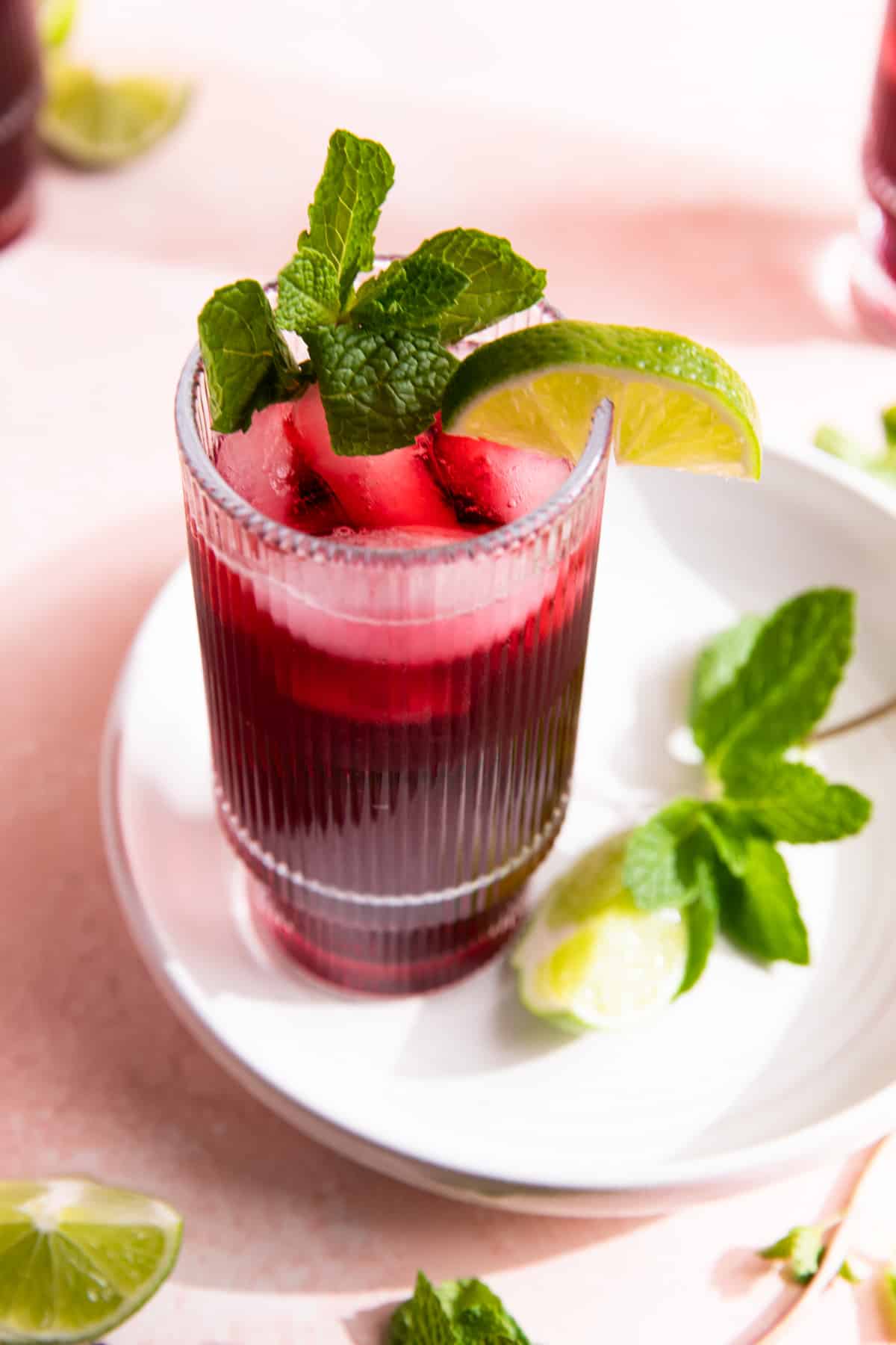Cup filled with agua de Jamaica on a white plate, garnished with lime and fresh mint.