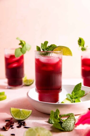 Glasses filled with a dark pink agua de Jamaica topped with lime slices and fresh mint leaves.