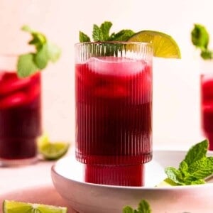 Glass filled with agua de Jamaica and topped with a lime wedge and a sprig of fresh mint.