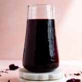 Carafe of homemade hibiscus syrup on white coasters.