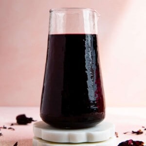 Carafe of homemade hibiscus syrup on white coasters.