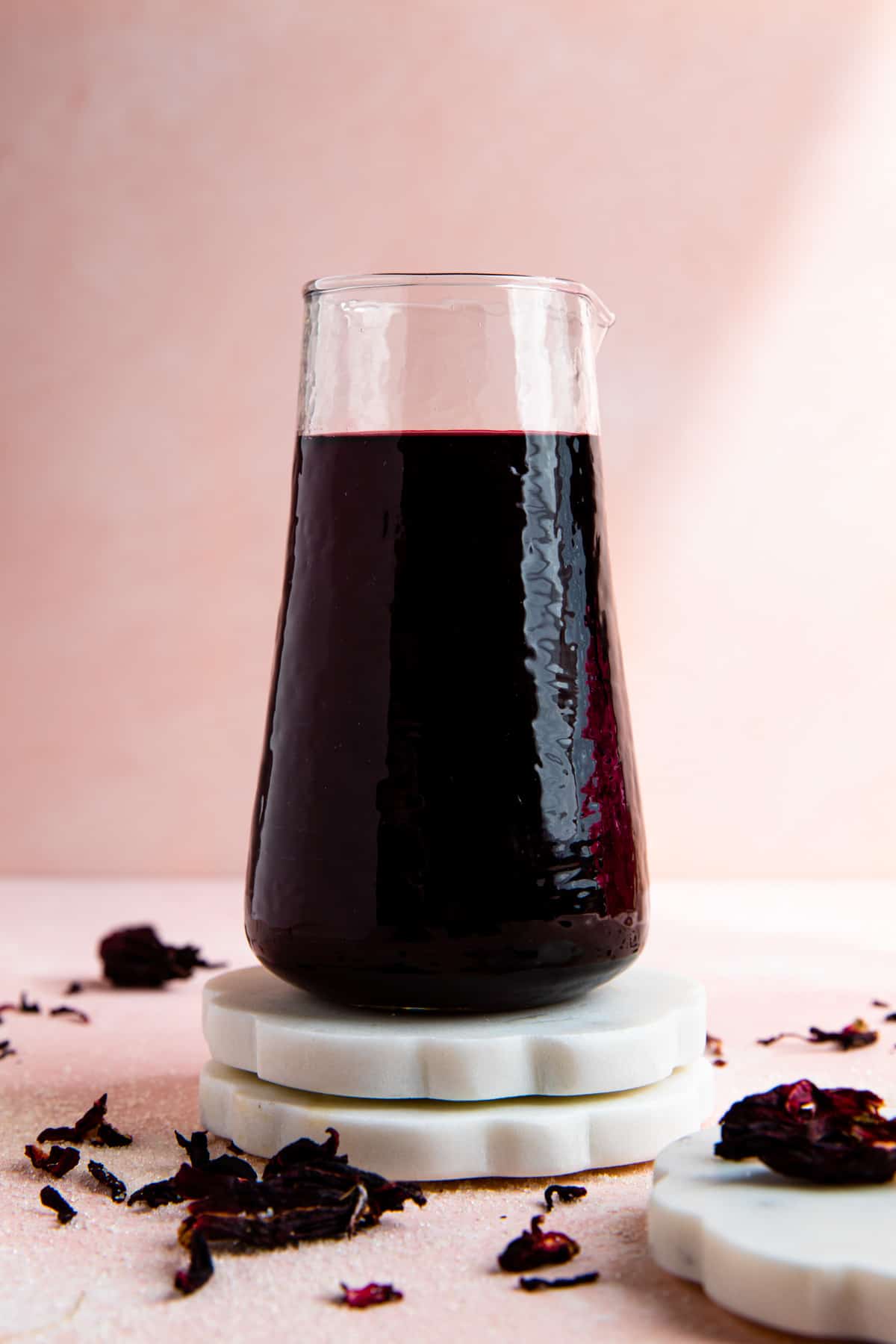 Carafe of homemade hibiscus syrup on white coasters.