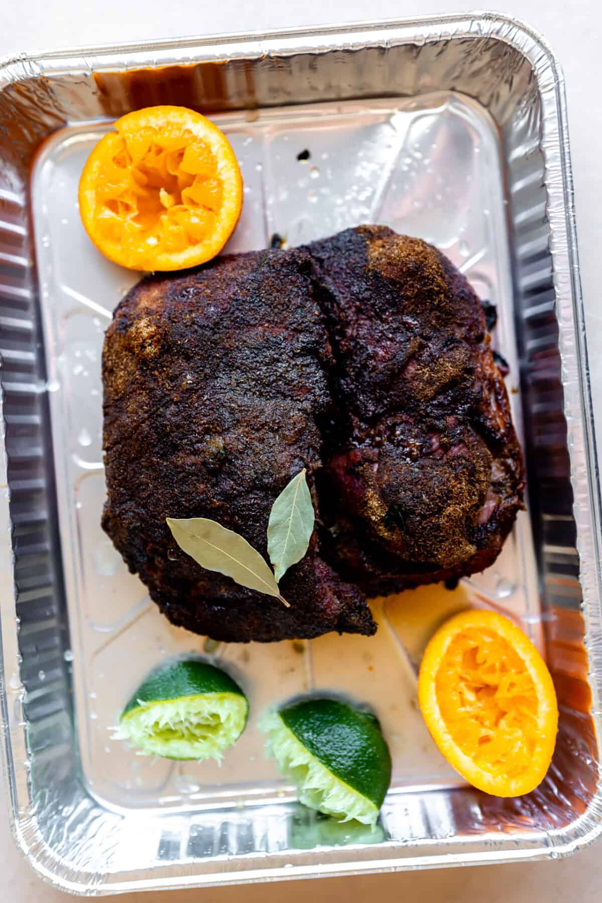 Smoked pork butt in a tin with bay leaves, limes, oranges for braising.