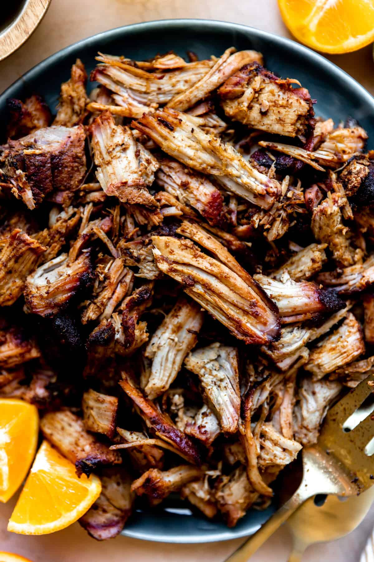 Up close view of smoked pork carnitas in a bowl with orange wedges, ready to serve for tacos.