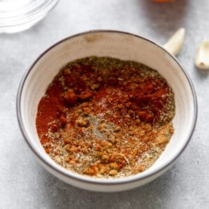 Bowl of carnitas seasoning mixed together with garlic cloves, jalapeno and an orange on the side.