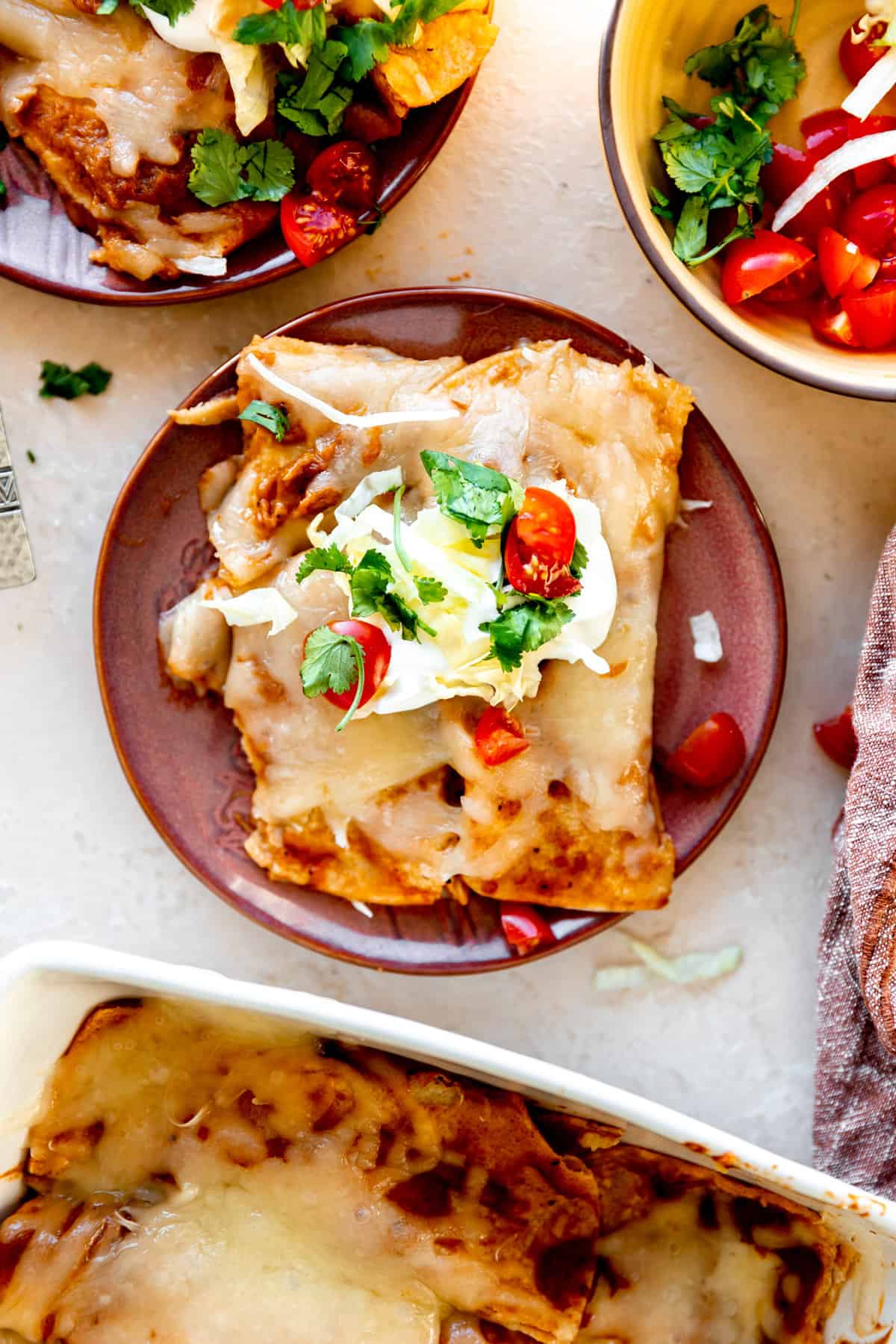 Plated cheese enchiladas topped with sour cream, cilantro and diced tomatoes. 