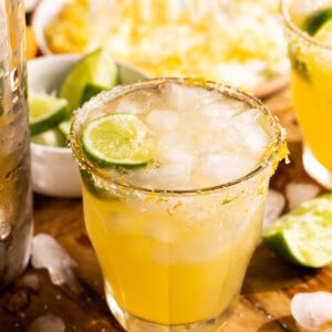 Glass filled with Texas margarita, garnished with a lime wedge, on a cutting board surrounded by sliced limes.